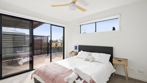 Une chambre avec un lit, une table de chevet, un ventilateur de plafond et une vue sur l’extérieur, accessible par une porte coulissante.