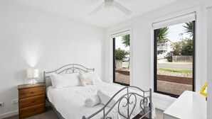Une chambre à coucher avec un lit, une table de chevet, une lampe et une fenêtre donnant sur l’extérieur.