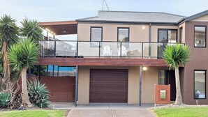 Une maison moderne à deux étages, dotée d’un garage, d’un balcon et d’un jardin bien entretenu.
