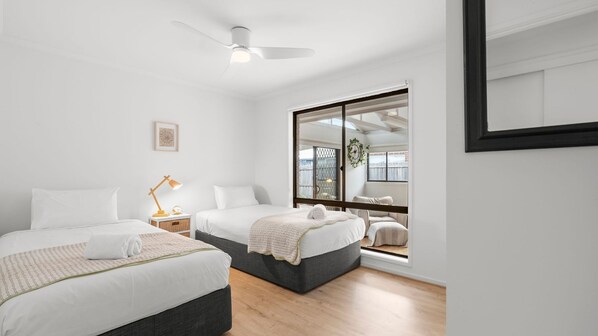 A modern bedroom with two beds, a ceiling fan, a large window with a view, and a framed picture on the wall.