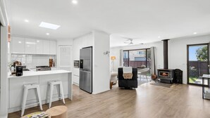 Une cuisine moderne avec des meubles blancs, un îlot central et un coin repas agrémenté d’une cheminée.