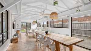 Une vaste terrasse dotée d’une table et de chaises en bois, d’un ventilateur de plafond et de plantes suspendues.