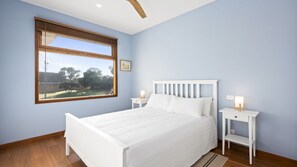 Un dormitorio con un ventanal grande, una cama blanca y dos mesitas de noche con lámparas.