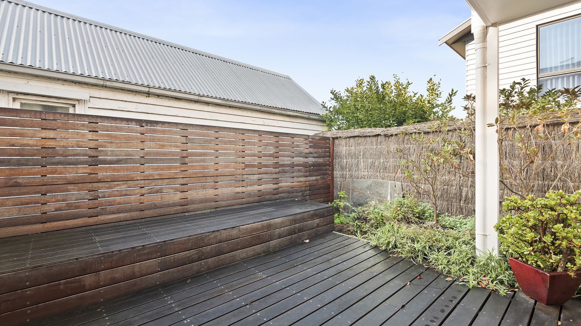 Une terrasse en bois avec un banc, un mur recouvert de chaume et un pot de fleurs.