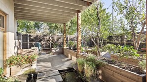 A covered patio area with raised garden beds, a small water feature, and a wooden fence in the background.