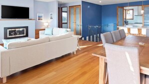 A modern living room with a sofa, TV, and dining area with a wooden table and chairs.