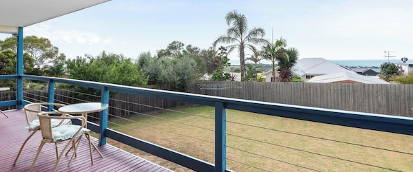 A balcony with a view of a grassy yard, a wooden fence, and a distant building.