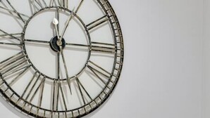 Ein Essbereich mit einem Holztisch, gedeckt für vier Personen, umgeben von Holzstühlen. Darüber an der Wand hängt eine große Wanduhr.