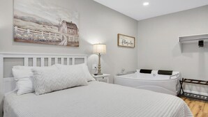 Ein Schlafzimmer mit einem großen Bett, einem Nachttisch mit Lampe, einem an der Wand montierten Fernseher und einer Badewanne.