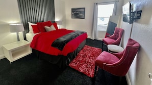Ein Hotelzimmer mit Bett, einem roten Sessel, einem kleinen Tisch und einem Fenster mit Vorhängen.
