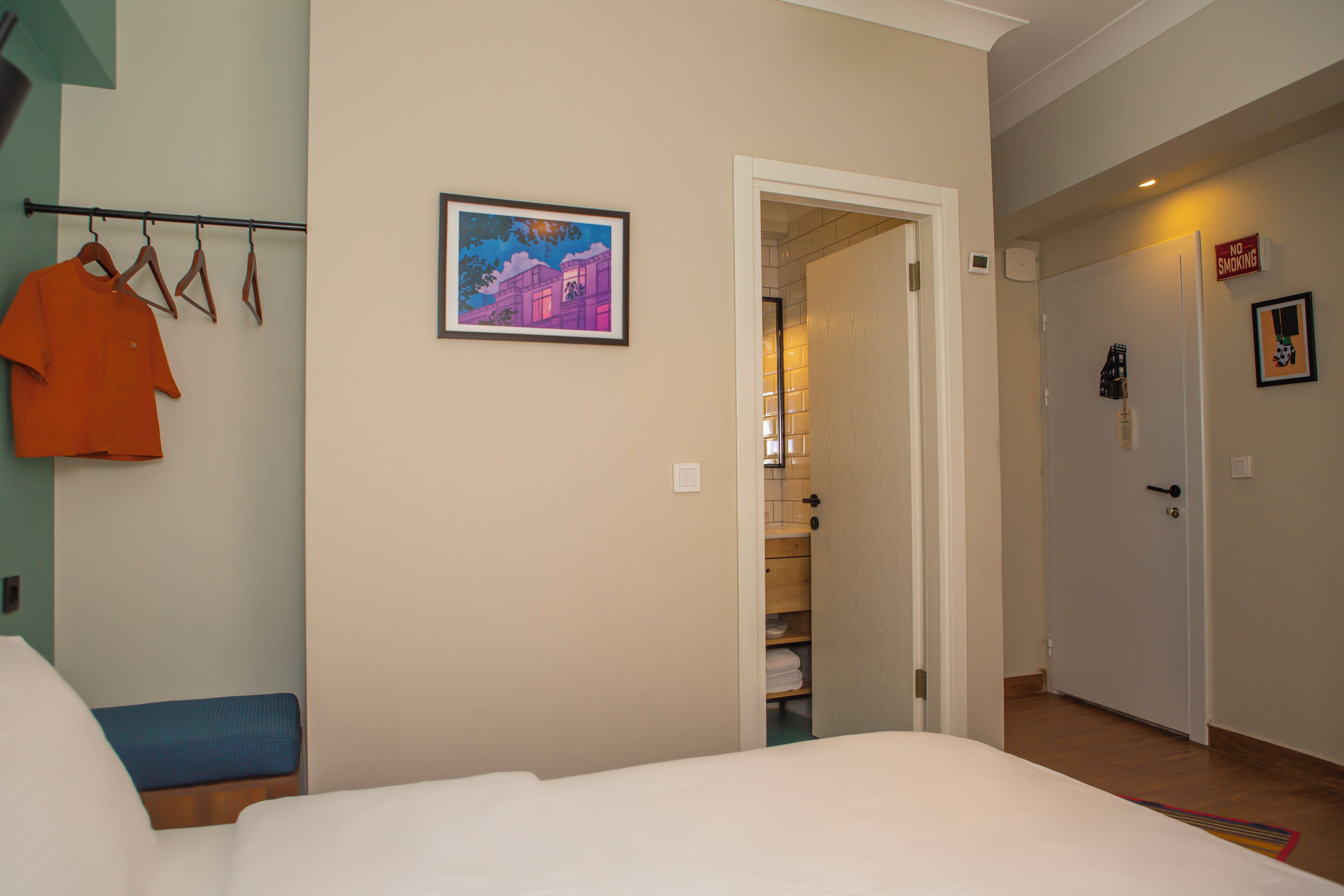 A hotel room with a bed, a hanging clothes rack, a framed picture on the wall, and a door leading to a bathroom.