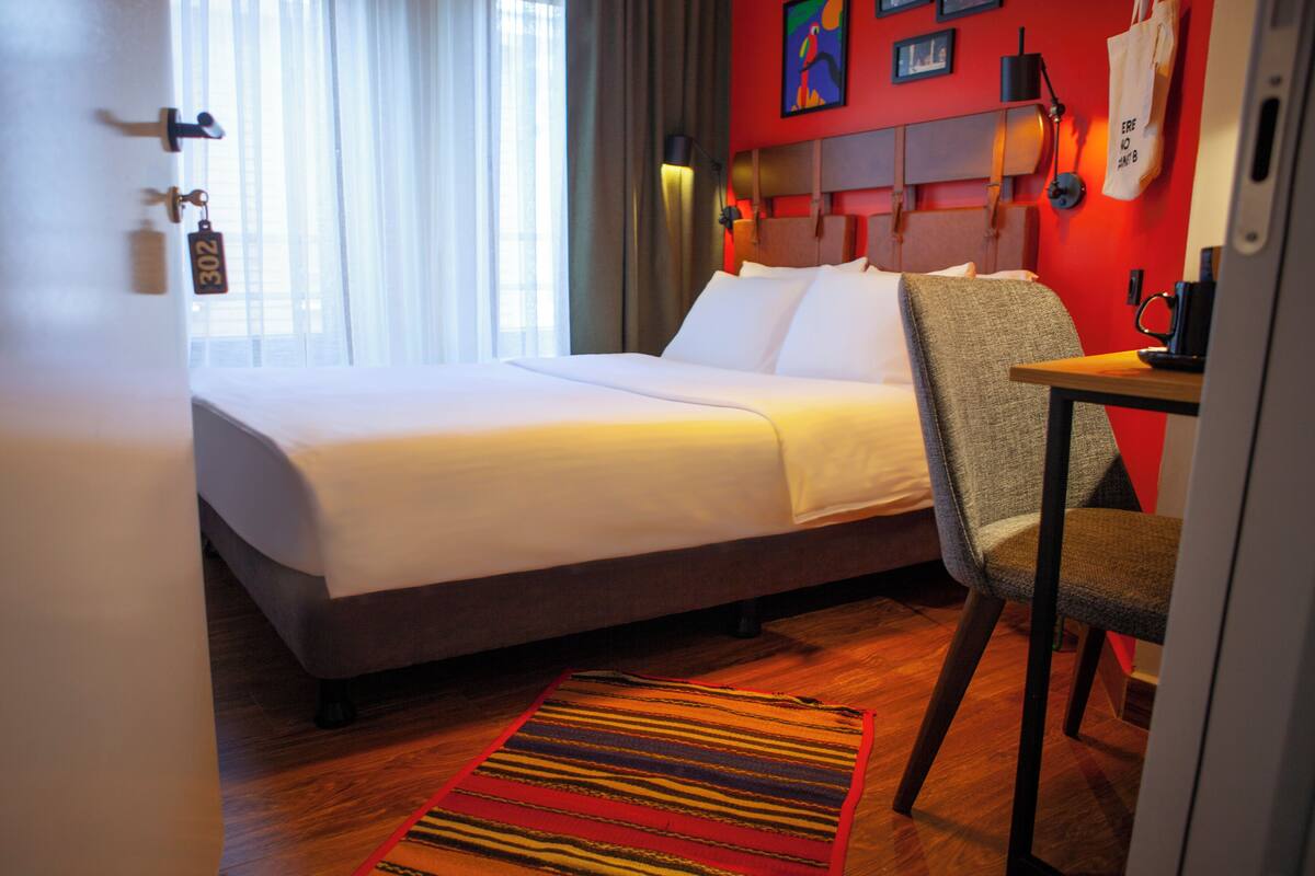 A hotel room with a bed, a chair, a desk, and a window with curtains.