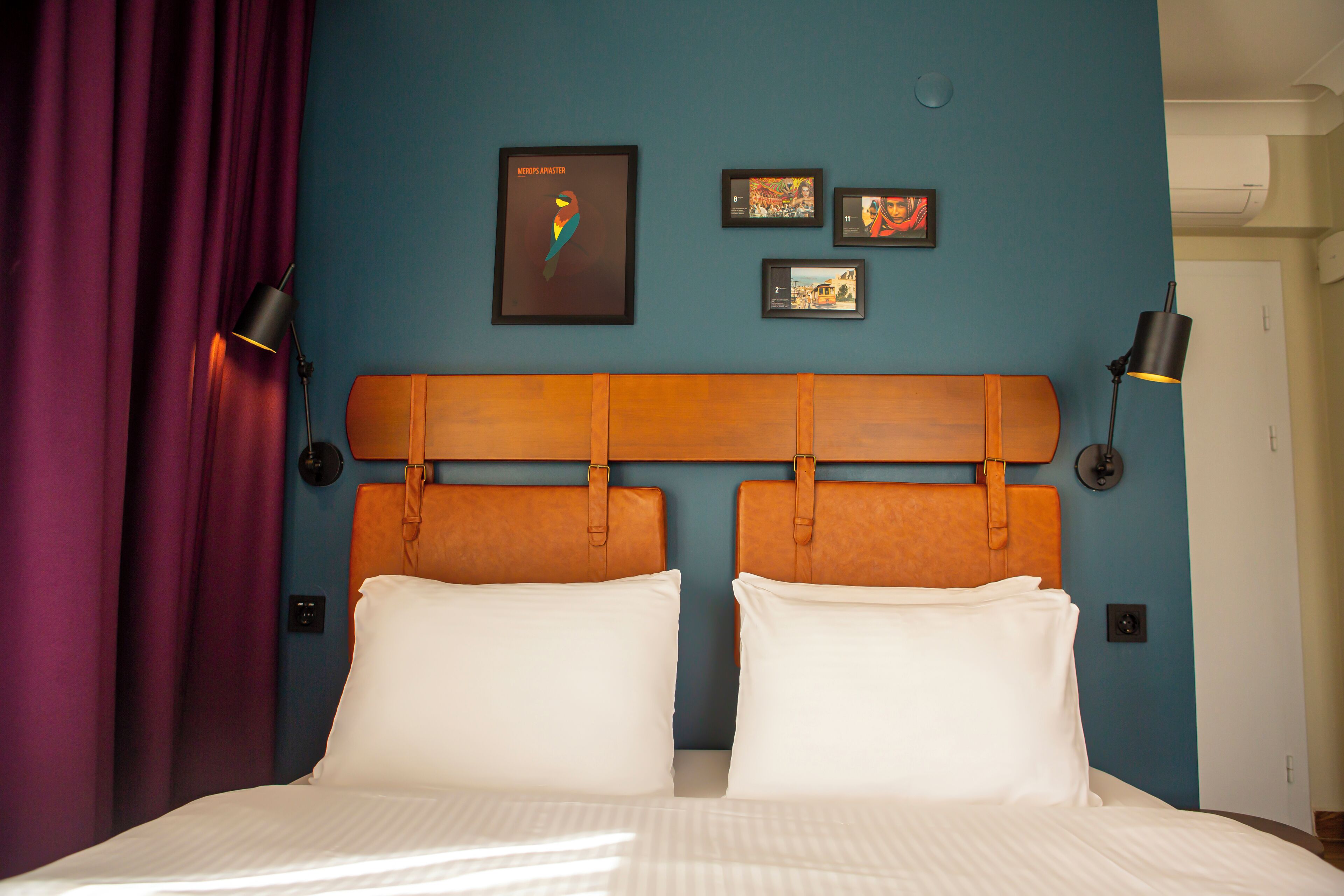 A double bed with white linens, a wooden headboard, and a blue wall with framed artwork.