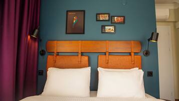 A double bed with white linens, a wooden headboard, and a blue wall with framed artwork.