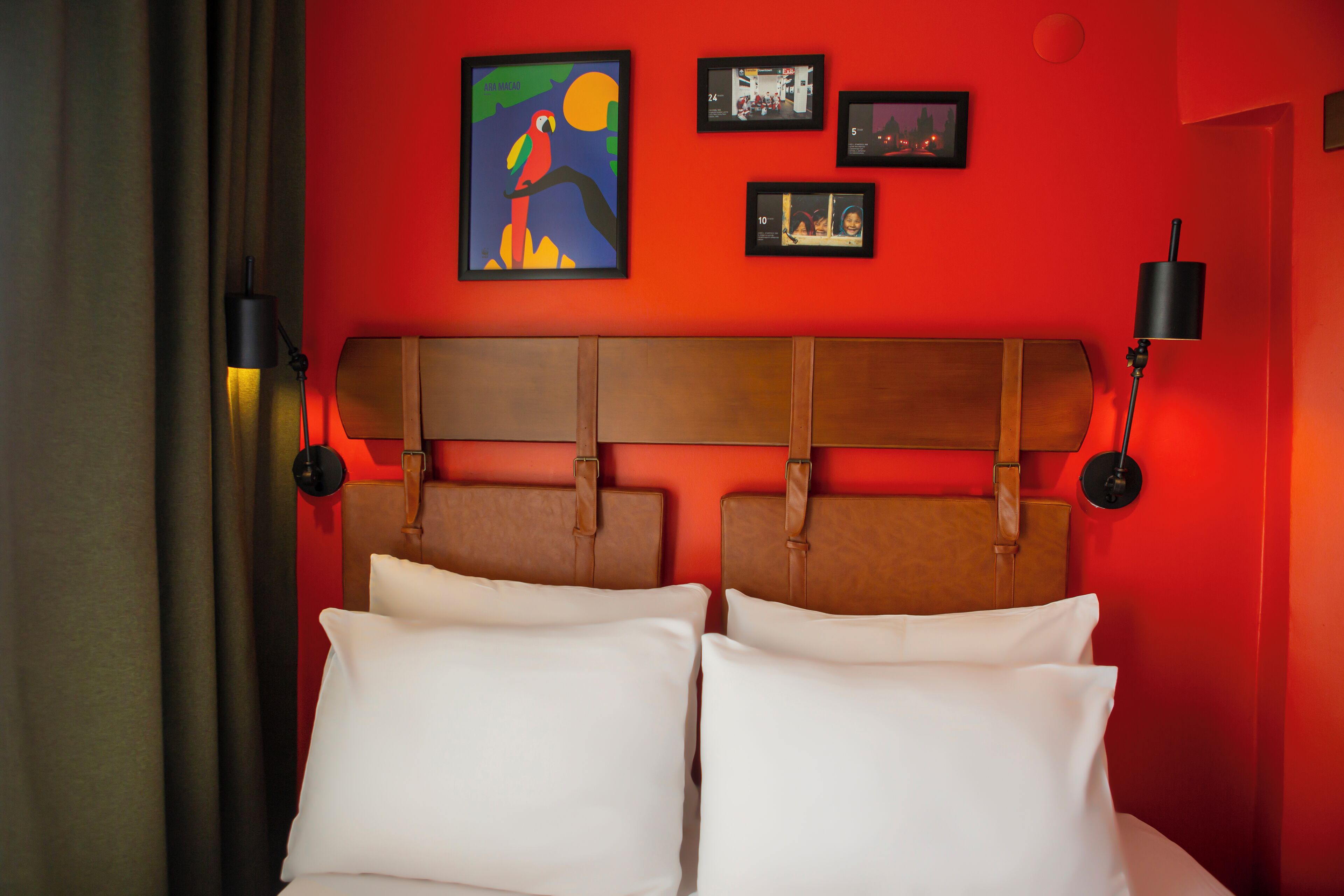 Ein Hotelzimmer mit roter Wand, einem Holzkopfteil, weißer Bettwäsche und gerahmten Bildern an der Wand.
