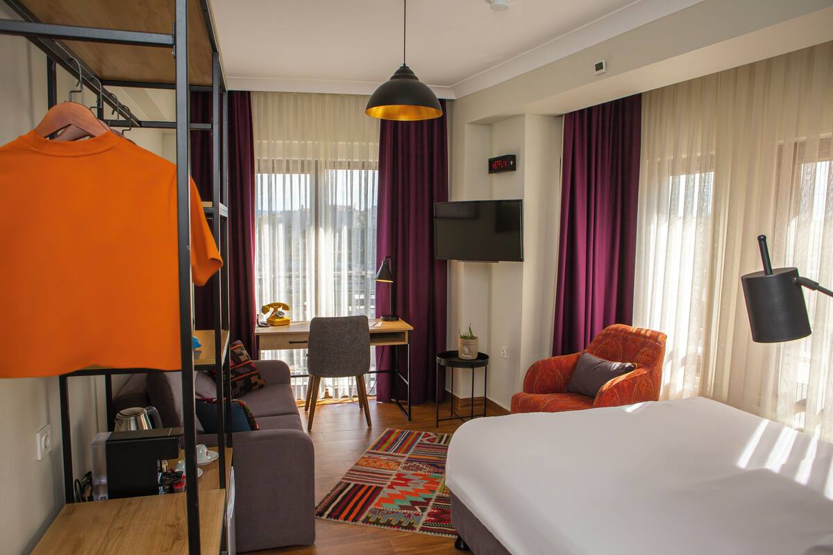 A hotel room with a bed, a desk, a chair, and a TV.