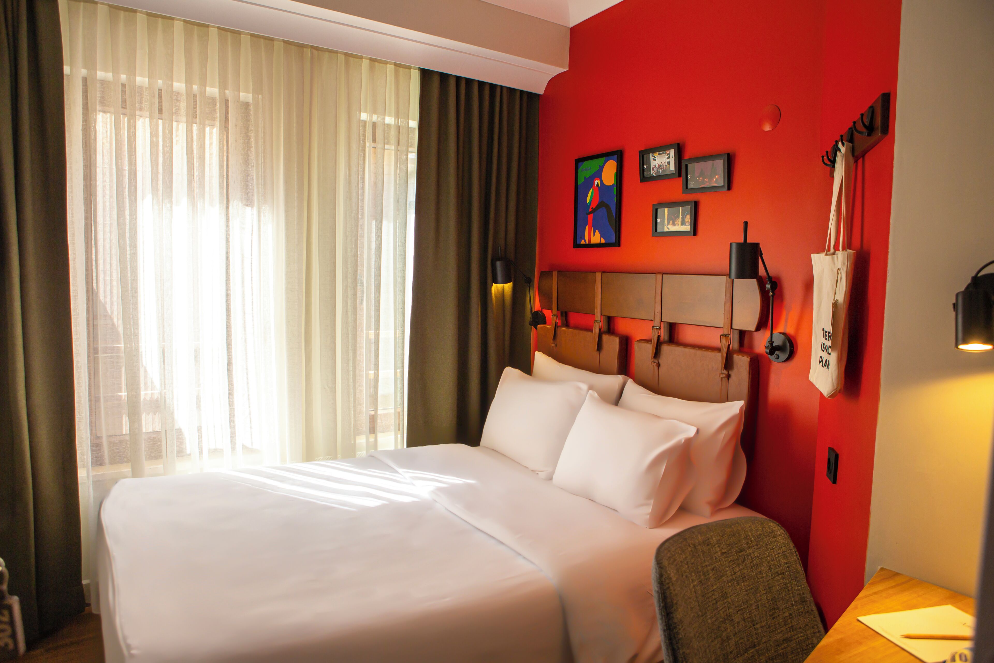 Une chambre d’hôtel avec un grand lit, une tête de lit dotée d’un luminaire, un téléphone fixé au mur et une fenêtre ornée de rideaux légers.