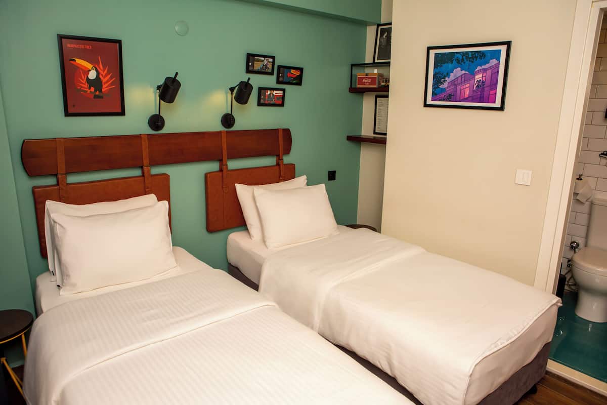 A room with two beds, a wooden headboard, a wall-mounted lamp, and framed pictures.