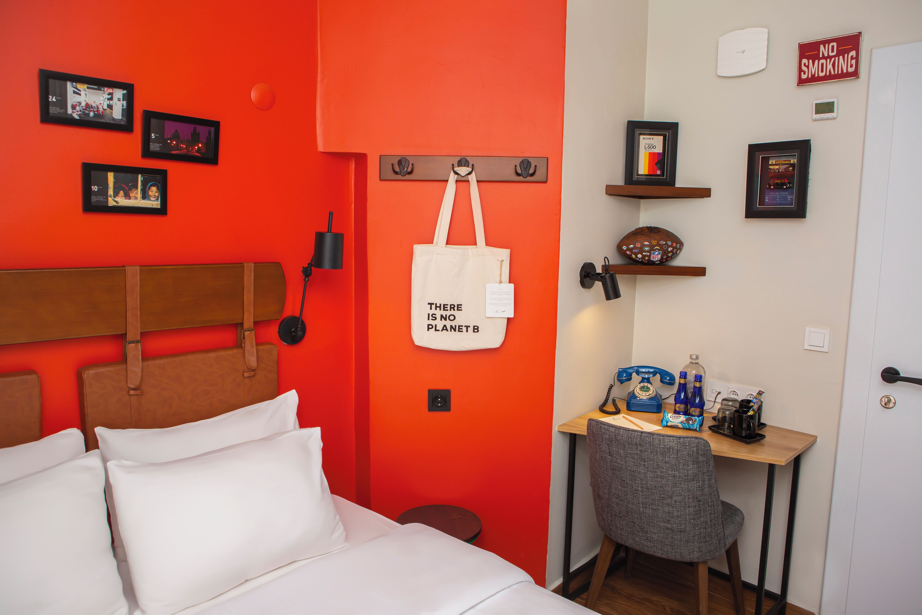 Una camera d'albergo con una parete rossa a contrasto, un letto con biancheria bianca, una scrivania con una sedia e un cartello 'No Smoking'.