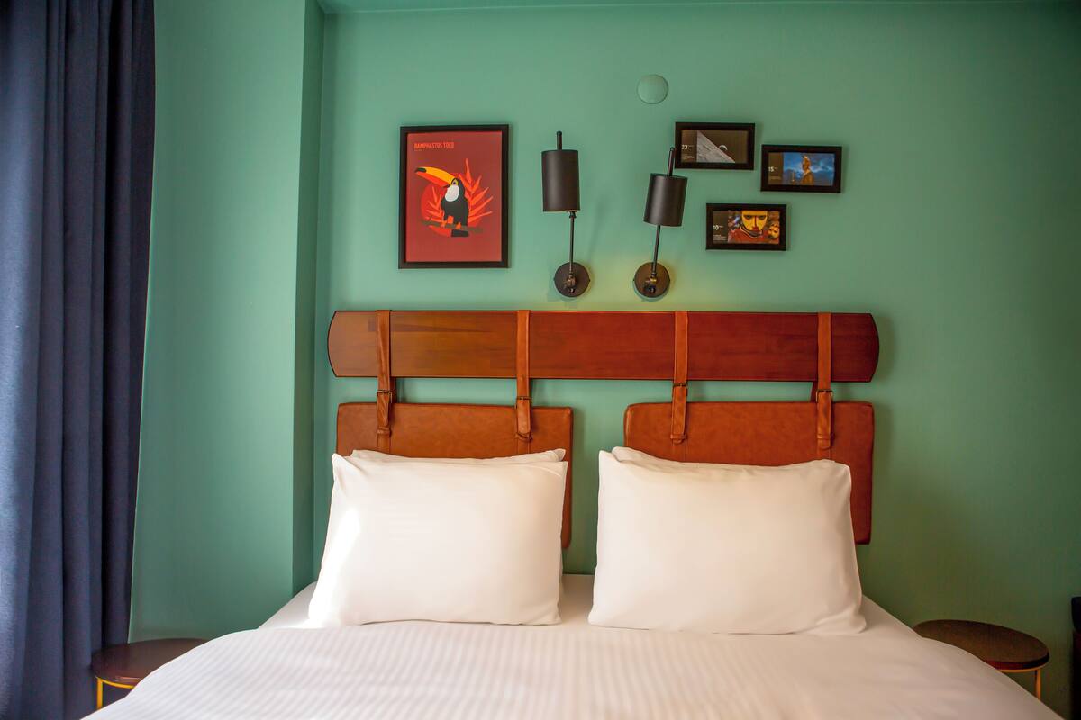 A hotel room with a bed, two pillows, a headboard, and a wall with framed pictures.