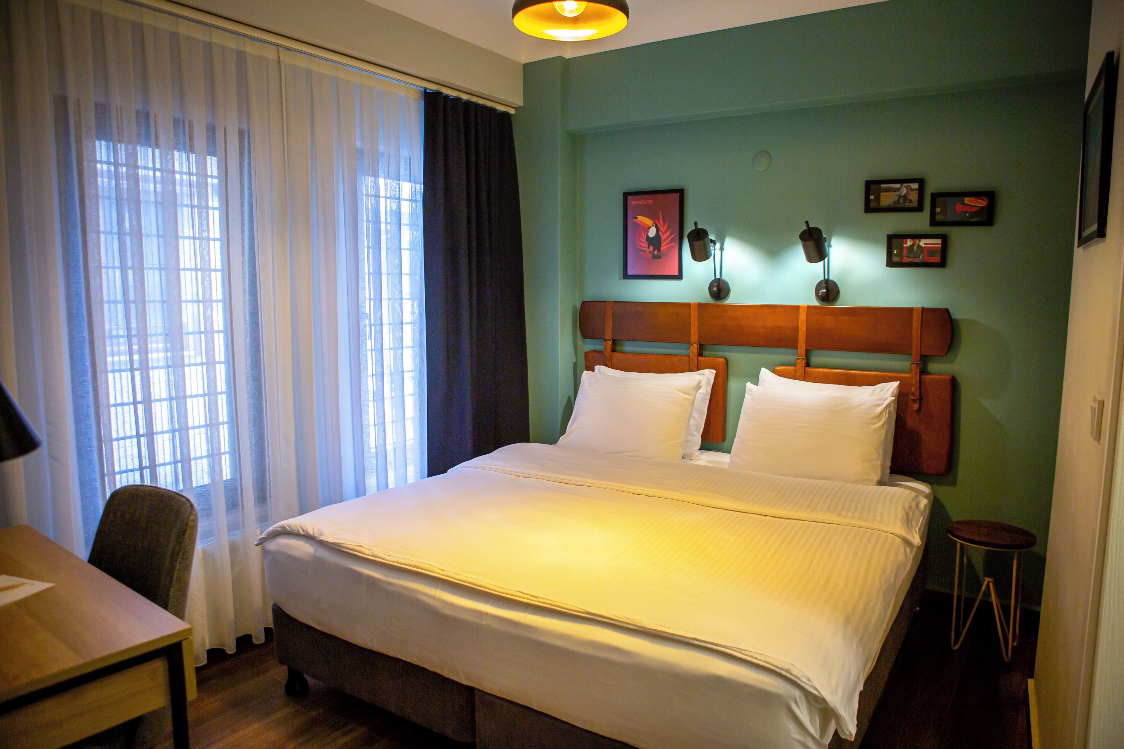 Quarto de hotel com cama, escrivaninha, cadeira e janela com cortinas.