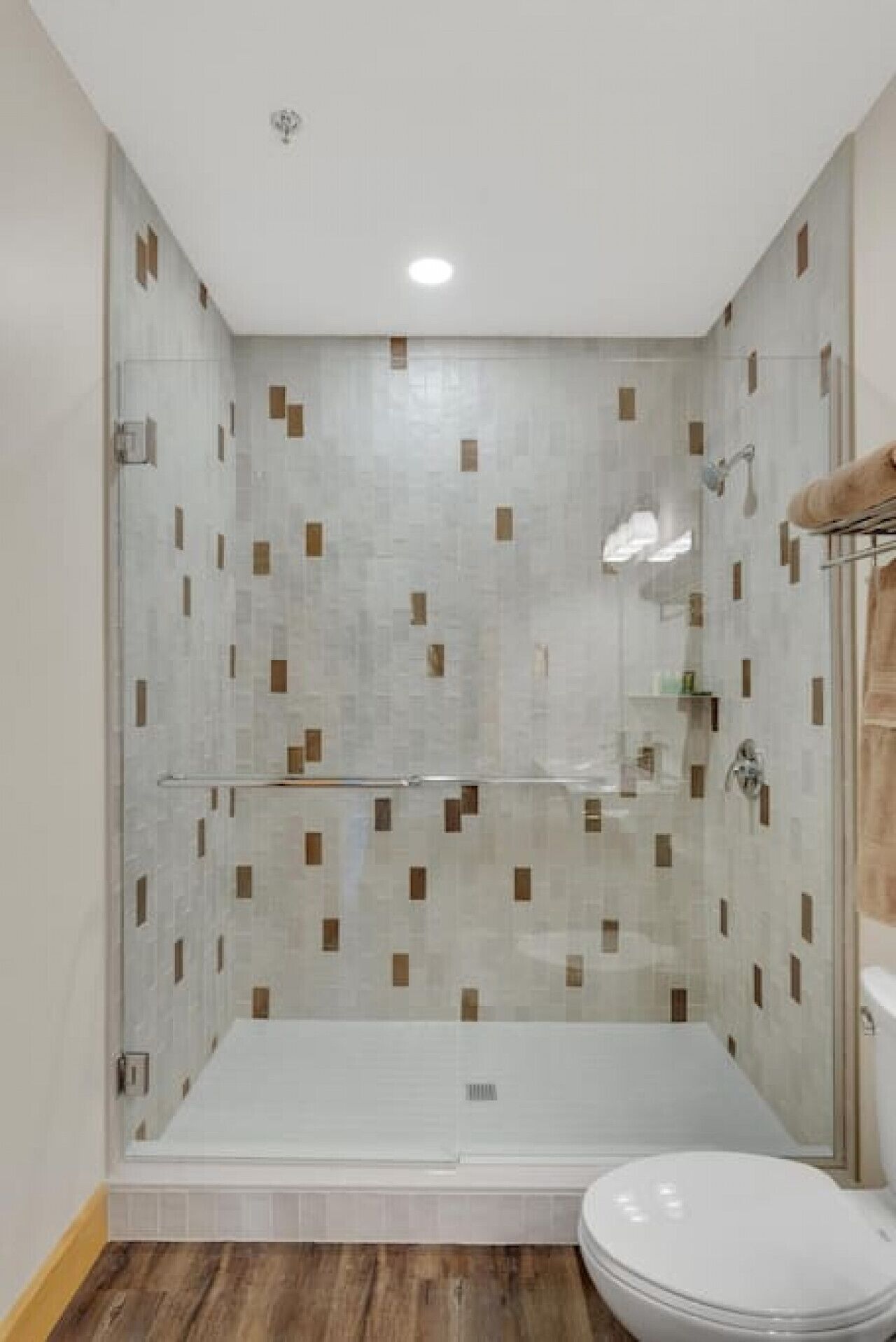 Ein modernes Badezimmer mit einer gläsernen Duschkabine, einer weißen Toilette und einem Holzboden.