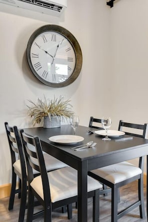 A dining area with a round table, black chairs, and a wall-mounted clock. - Romantic Getaway with Private Patio and Hot Tub on Main Street - Maple Suite (Berlin)