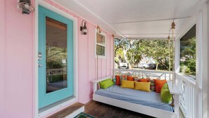 A porch with a white swing bed, a turquoise door, and a pink wall. - Tutti Frutti (Santa Rosa Beach)