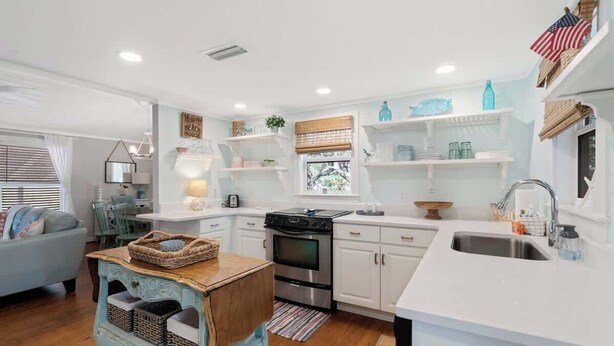 A modern kitchen with white cabinetry, a built-in oven, and a sink. There is a dining area with a table and chairs, and a decorative wall sign. - Tutti Frutti (Santa Rosa Beach)