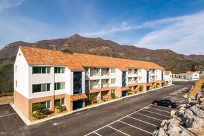 A multi-story hotel with a tiled roof, parking lot, and mountainous backdrop.