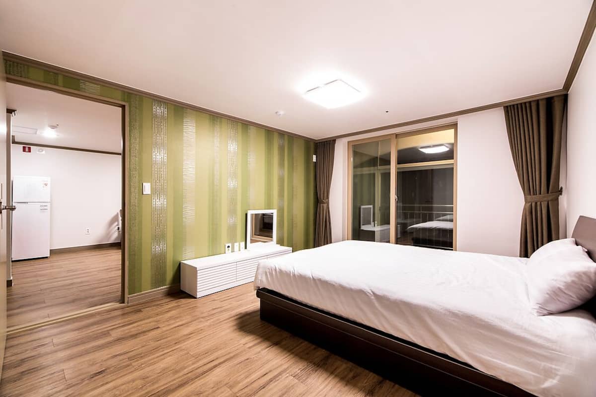 A modern bedroom with a large bed, a mirror, a TV, and a sliding door leading to a bathroom.