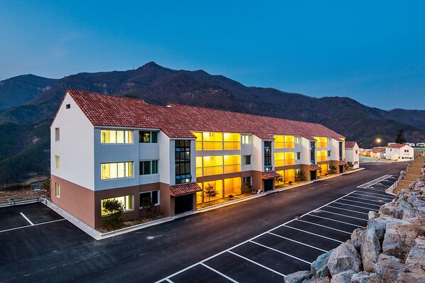 A multi-story hotel with a red-tiled roof, large windows, and a parking lot in front.