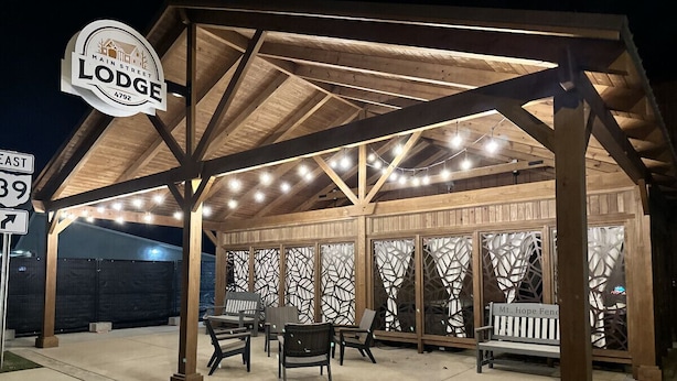 A covered outdoor seating area with string lights, wooden furniture, and a sign reading "Main Street Lodge 4792".