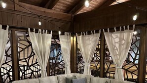 A cozy seating area with a sectional sofa and a coffee table, surrounded by wooden beams and patterned curtains.