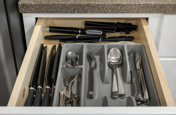 A drawer with neatly organized cutlery and utensils, including knives, forks, spoons, and a black pen.