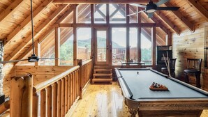 A wooden interior with a pool table, wooden railings, and a view of the outdoors. - Updated Cabin | Amazing Views,Hot Tub,Location (Sevierville)