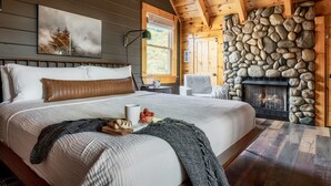 A bedroom with a large bed, a stone fireplace, a window with a view, and a painting on the wall. - Updated Cabin | Amazing Views,Hot Tub,Location (Sevierville)