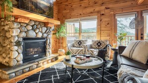 A cozy cabin interior with a stone fireplace, wooden walls, and a comfortable seating area with a coffee table. - Updated Cabin | Amazing Views,Hot Tub,Location (Sevierville)