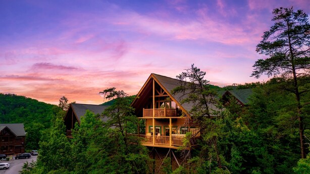 A cabin with a balcony, surrounded by dense forest, and a road in the foreground. - Updated Cabin | Amazing Views,Hot Tub,Location (Sevierville)