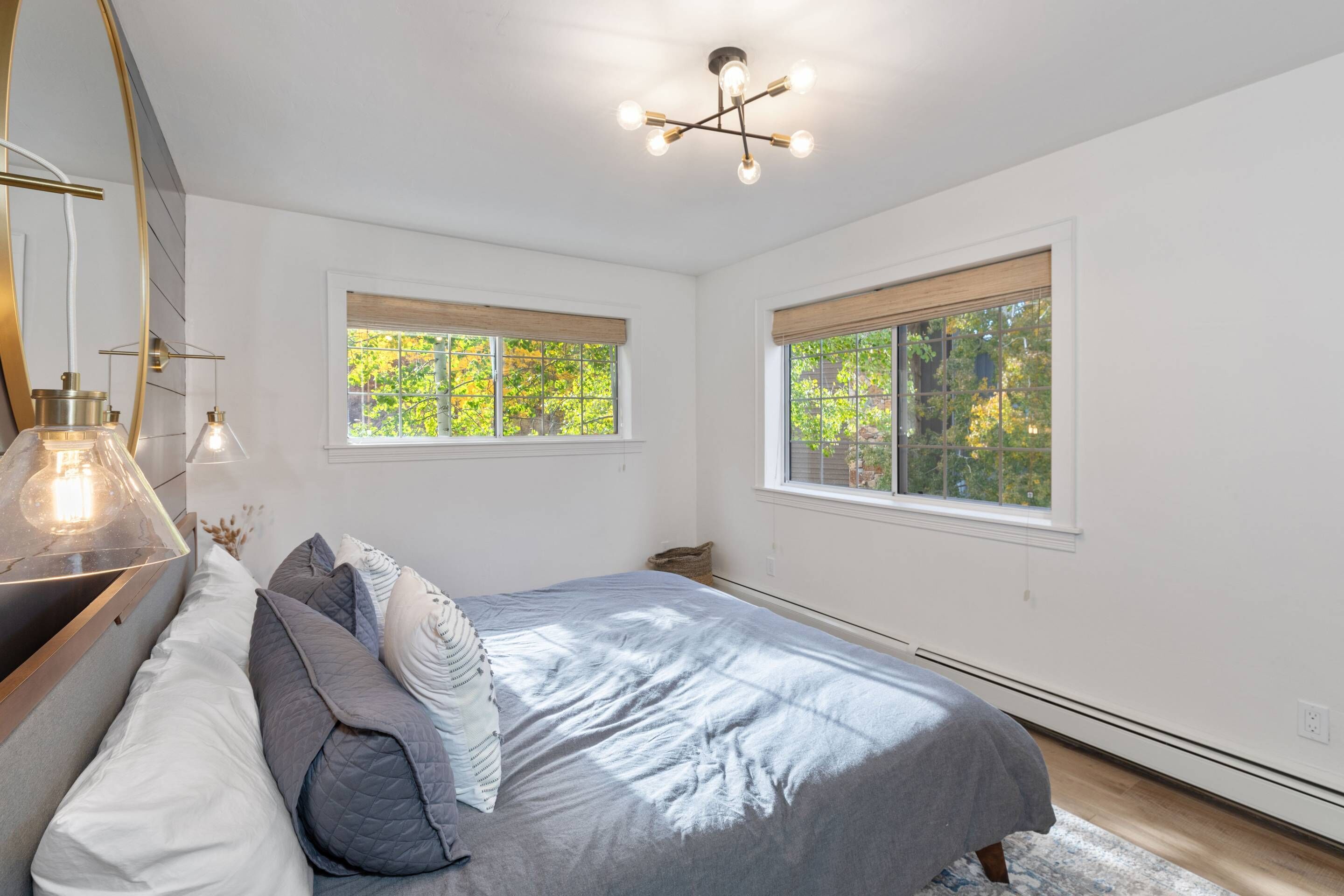 Une chambre à coucher avec un lit, deux fenêtres, un luminaire au plafond et un radiateur.