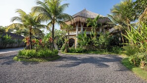 Een tropisch resort met een gebouw met rieten dak, omgeven door weelderige begroeiing en palmbomen.