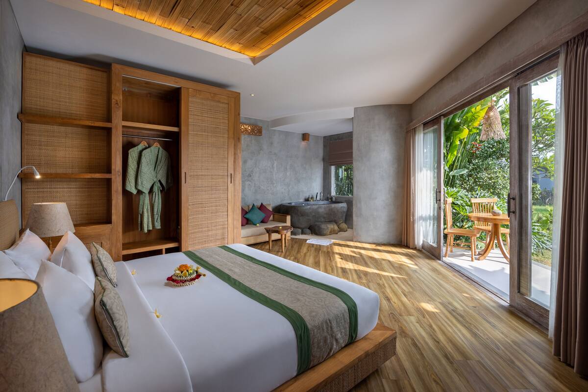 A spacious bedroom with a large bed, wooden wardrobe, and a view of the garden through large windows.