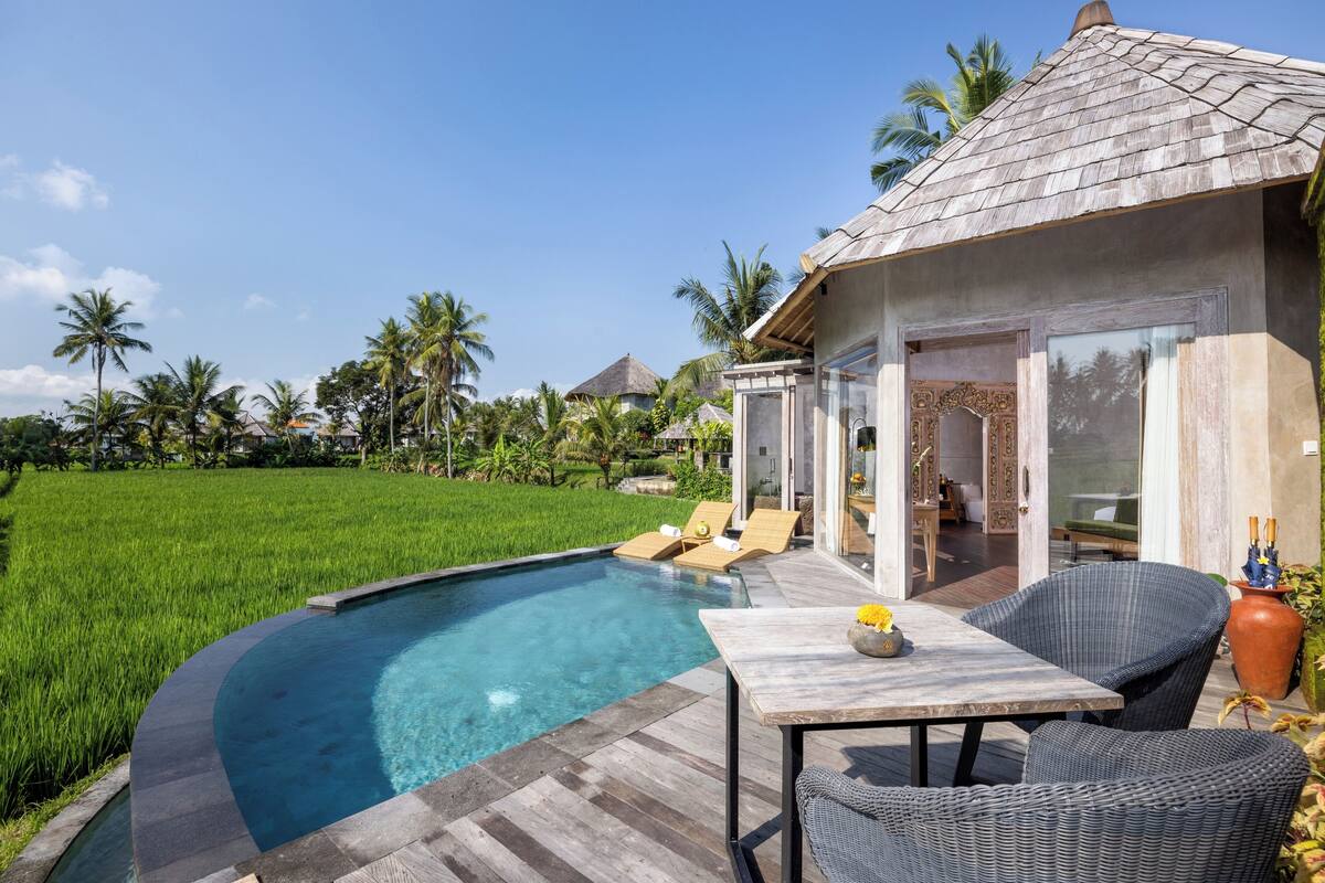 A poolside area with a wooden deck, lounge chairs, and a table with a vase.
