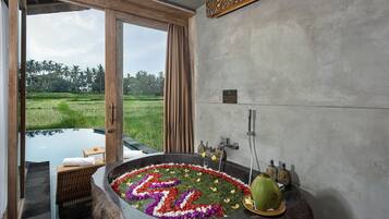 A bathroom with a large bathtub surrounded by flowers, a shower, and a view of a green landscape.