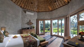 Een ruime slaapkamer met een groot bed, een houten plafond en uitzicht op een weelderige tuin door grote ramen.