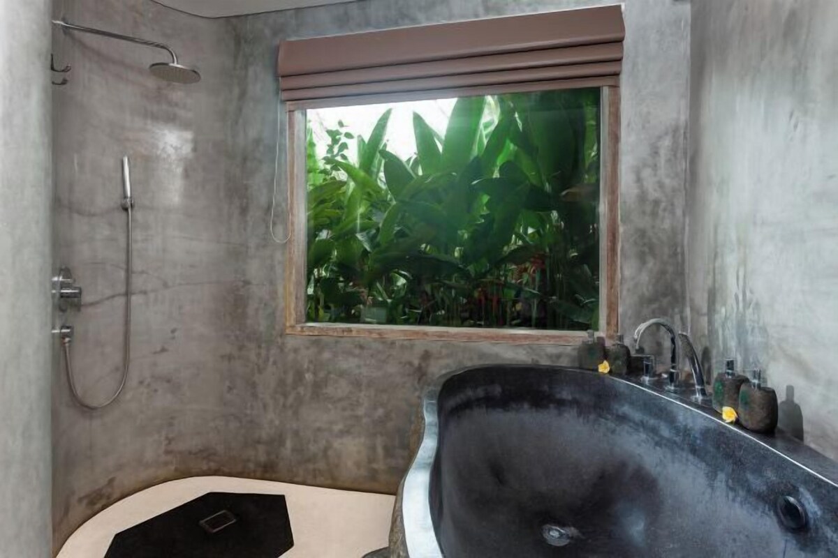 Une salle de bain avec un grand lavabo noir, une douche et une fenêtre donnant sur un paysage verdoyant.