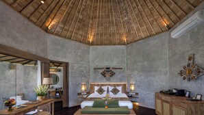 Een ruime slaapkamer met een groot bed, houten plafond en een klein bureau met spiegel en lamp.
