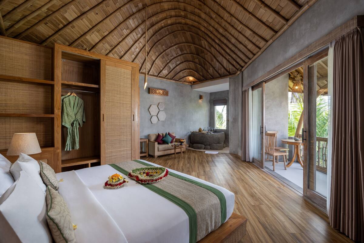 A spacious bedroom with a large bed, a wardrobe, a sofa, and a balcony with a view of greenery.
