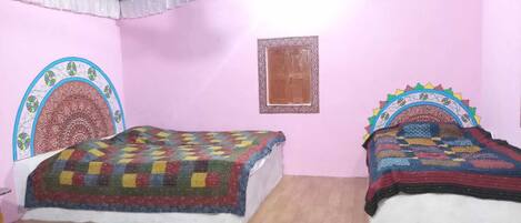 A room with two beds, each with a colorful quilt, a small window, and a decorative headboard.