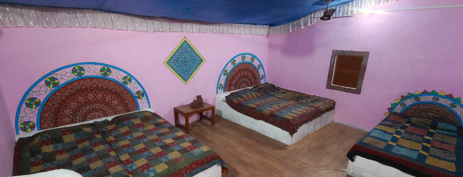 A room with three beds, each with a patterned bedspread. There is a small table and a wall hanging.